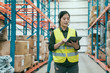 © PR Image Factory - Businesswoman using digital tablet in distribution warehouse. young woman staff in headset talking to customer online while walking in large storehouse. female colleague in background check inventory