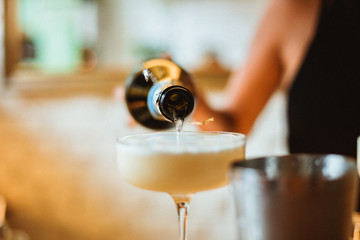 Wall Mural - Bartender adding champagne on top of a cocktail in a beautiful glass. Selective focus lifestyle photo with film grain effect