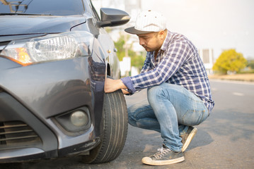 Young man changing wheel on the car at the side of the road, young businessman has problems with the wheel of car. He is kneeing and looking at it with seriousness , Transportation, traveling concept