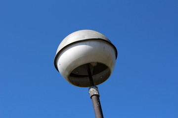 Vintage retro old dilapidated white round street light lamp mounted on metal pole on clear blue sky background