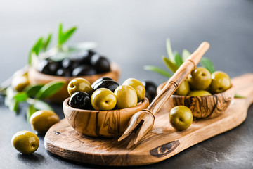 Wall Mural - Fresh olives in bowl on dark stone table. Olive wood picker on rustic board.