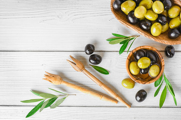 Wall Mural - Fresh green and black olives in rustic bowl on white table. Ripe olive with leaves on light background.