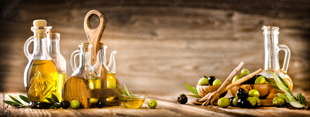 Fresh olives in rustic bowls on old wooden table. Virgin olive oil in clear glass bottles copy space.  Panorama or banner concept. - obrazy, fototapety, plakaty 