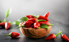 Red Hot Peppers In Wooden Bowl On Dark Stone Table. Chili Spiced Small Pepper And Leaves.