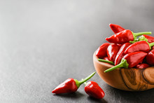 Hot Pepper In Wooden Bowl On Dark Stone Table. Chili Red Peppers And Green Leaves On Black Background.