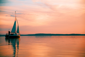 Sailing boat floats on the lake at sunset.