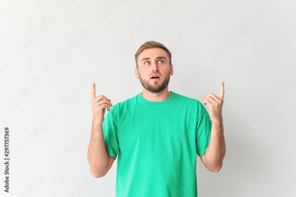 Surprised young man pointing at something on light background