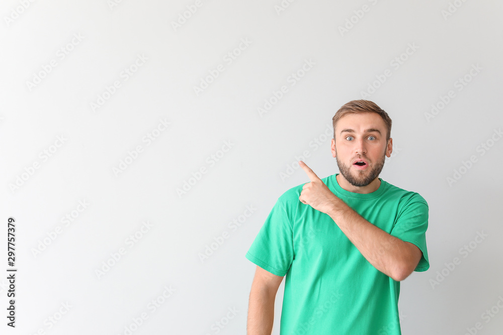 Surprised young man pointing at something on light background