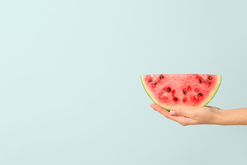 Female hand with piece of juicy watermelon on color background