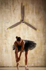 Wall Mural - Full body portrait. Russian ballerina in a black dancing suit is posing in dark studio