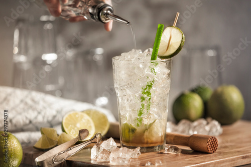 A glass of caipirinha on a wooden board with limes and crushed ice as decoration. A fresh traditional Brazilian cocktail with citrus fruits and rum.