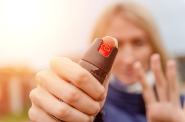 Blonde holds pepper spray for self-defense close-up outside in the afternoon