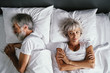 © luengo_ua - Overhead of senior couple in the bed. Pretty aged woman is angy with her sleeping husband.