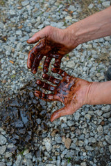 Caucasian hands stained with black gasoline on stones background