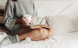 girl in home clothes on the couch reads a book and drinks a hot drink