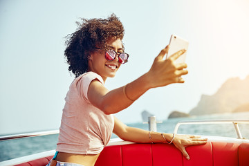 Wall Mural - Smiling young woman sitting on a boat taking selfies