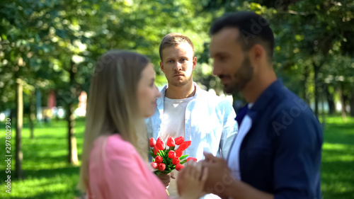 Cuadros en Lienzo Disappointed man with flowers looking at girlfriend flirting with another man