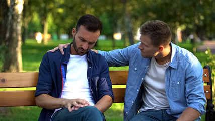 Wall Mural - Young male supporting friend sitting outdoors together, friendship care, advice