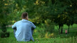 © motortion - Young man sitting grass park enjoying weekend free time, loneliness, back view