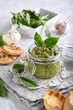 traditional italian basil pesto sauce in a glass jar wiht toasts on a light stone table