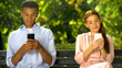 © motortion - Male and female teenagers sitting on bench and chatting on smartphones, problems