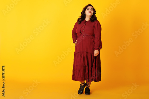 Fotografía Attractive south asian woman in deep red gown dress posed at studio on yellow background