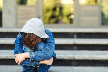 Depressed boy sitting alone with sad feeling outside school. Schoolboy sits at stairs and crying. School bullying concept