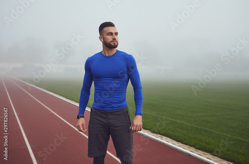 Fotografía A male athlete in training stands at the stadium in the fog.