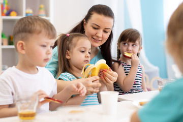 Wall Mural - kindergarten teacher and preschoolers kids having break for fruits and vegetables