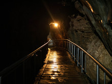 A Wet Wooden Walkway Bridge Through A Dark Lit Cave