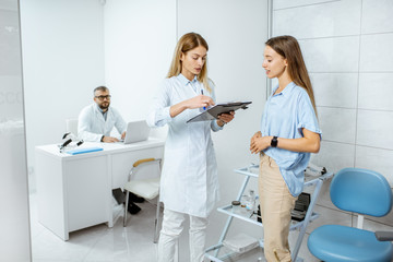 Wall Mural - Young patient with female doctor during a medical consultation standing at the ENT office with senior doctor on the background