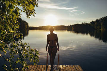 Young woman going into the lake from pier at sunset after sauna in Finland