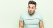 © Asier - Young handsome man against a green background shrugs shoulders and open eyes confused.