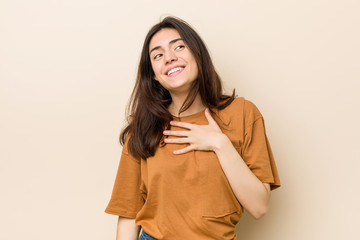 Wall Mural - Young brunette woman against a beige background laughs out loudly keeping hand on chest.