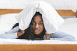 © Prostock-studio - Young sad black woman in bed covering head with pillow
