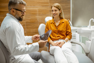 Wall Mural - Beautiful woman as a patient with senior dentist during a medical consultation at the dental office, doctor showing x-ray image of a jaw