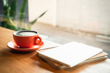 Orange coffee cup Or hot espresso And a notebook on a wooden table in a coffee shop