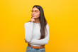 © Asier - Young pretty arab woman against a yellow background looking sideways with doubtful and skeptical expression.