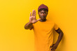 © Asier - Young black man wearing rastas over yellow background standing with outstretched hand showing stop sign, preventing you.