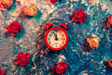 Time Concept. Red Vintage Alarm Clock And Faded Rose Buds On Smeared Blue And White Paint. Abstract Art Background.