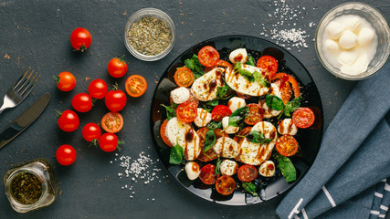 Wall Mural - Italian caprese salad with chopped tomatoes, mozzarella cheese, basil, spices, balsamic vinegar and olive oil. Vegetarian dish. dark concrete background