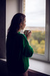 © saulich84 - woman in a green sweater holds a metal mug of cocoa