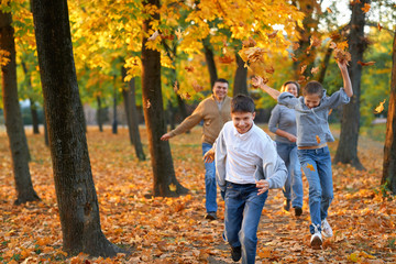 Happy family having holiday in autumn city park. Children and parents running, smiling, playing and having fun. Bright yellow trees and leaves