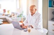 © Krakenimages.com - Senior handsome man smiling happy and confident. Sitting using laptop and drinking cup of coffee at home