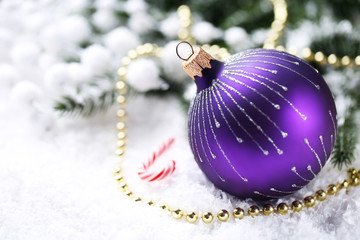 Christmas bauble with beads, candy and fir tree branches on white snow