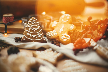 Wall Mural - Festive gingerbread man and christmas tree cookies on background of wooden rolling pin, anise, cinnamon, pine cones, golden lights bokeh on rustic table. Merry Christmas. Atmospheric