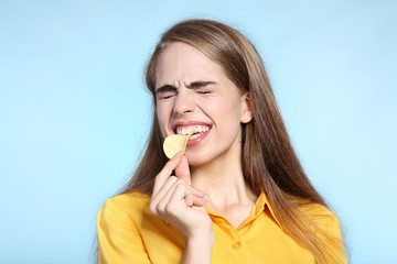 Young beautiful girl eating potato chip on blue background