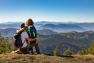 Wall Mural - rear view of hikers couple with backpack sitting on top of the mountain and enjoying the view during