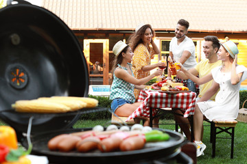 Wall Mural - Group of friends at barbecue party outdoors. Blurred view of grill with sausages and vegetables