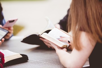 Closeup shot of females sitting around a table and reading the bible